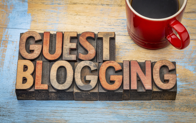 Wooden Letters forming the word Guest Blogging on a Wooden Table with a Red Cup of Coffee.